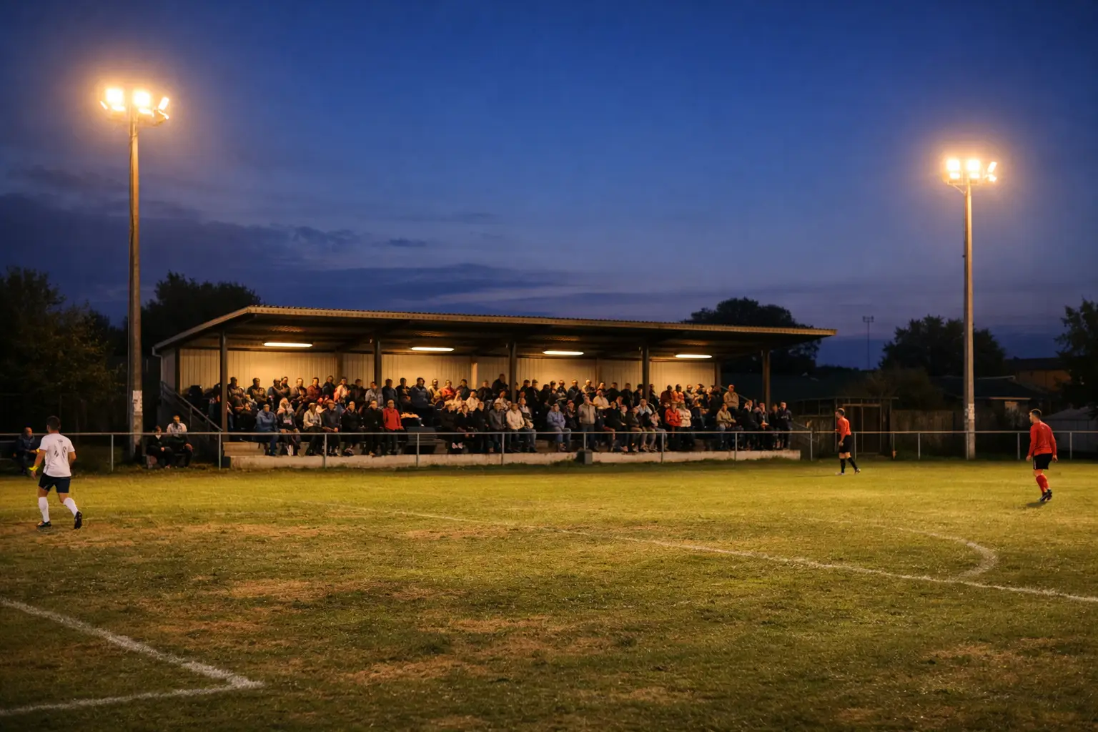 Kleines Fußballstadion mit niedriger Tribüne und Flutlicht bei Abenddämmerung